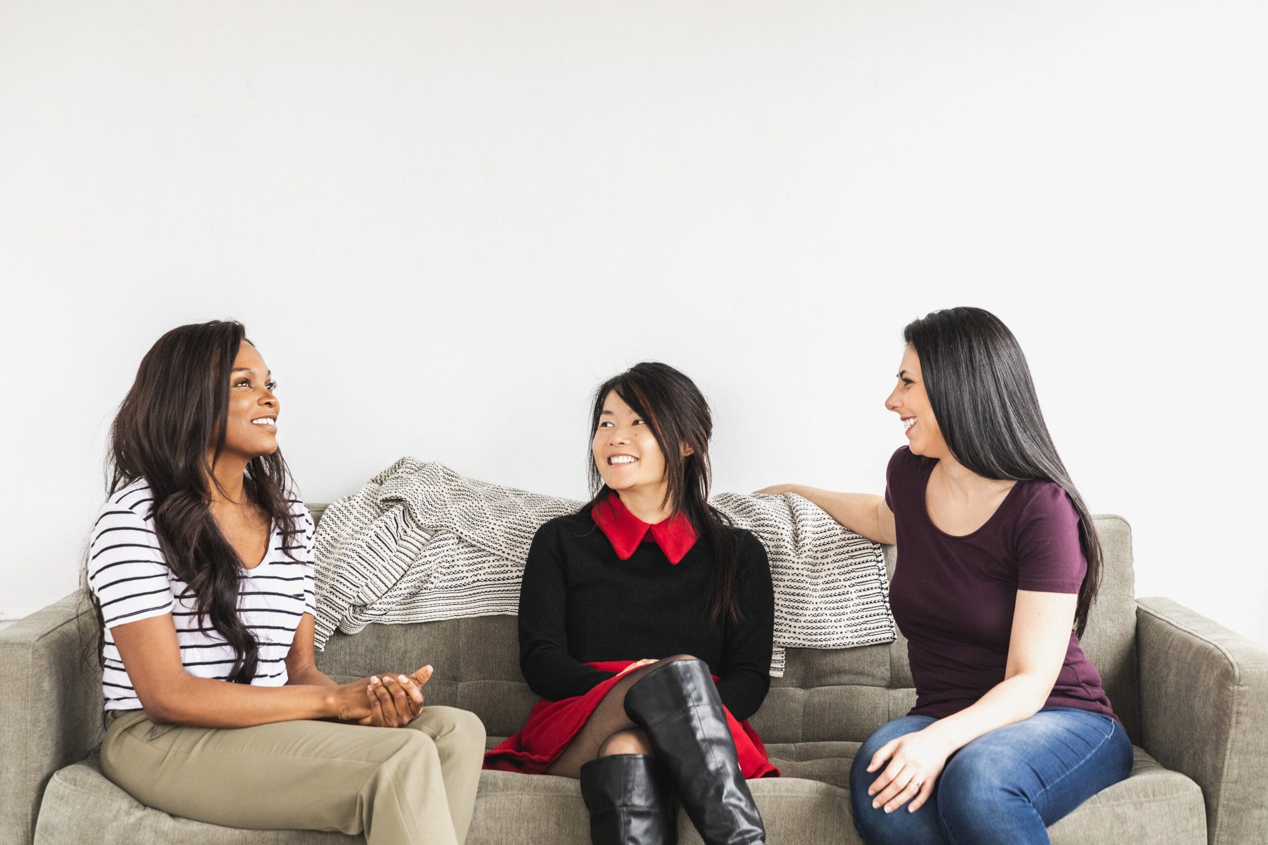 Three women talking on a grey sofa