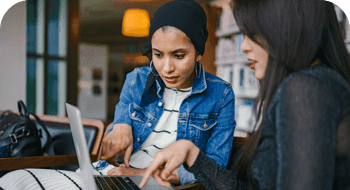 Two women sitting on couch referring to laptop