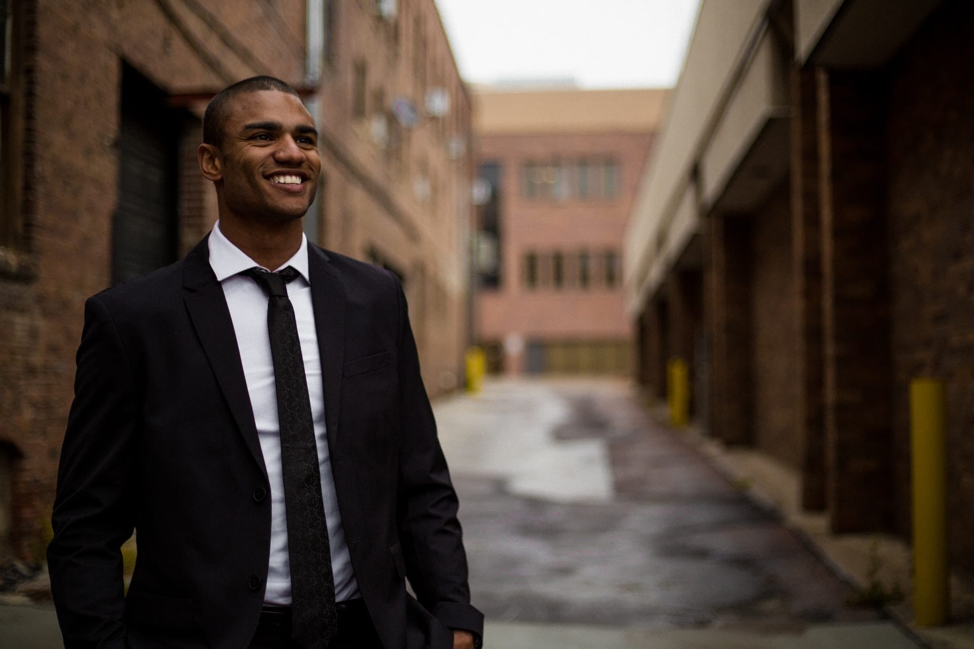 Smiling man in suit and tie near brick building