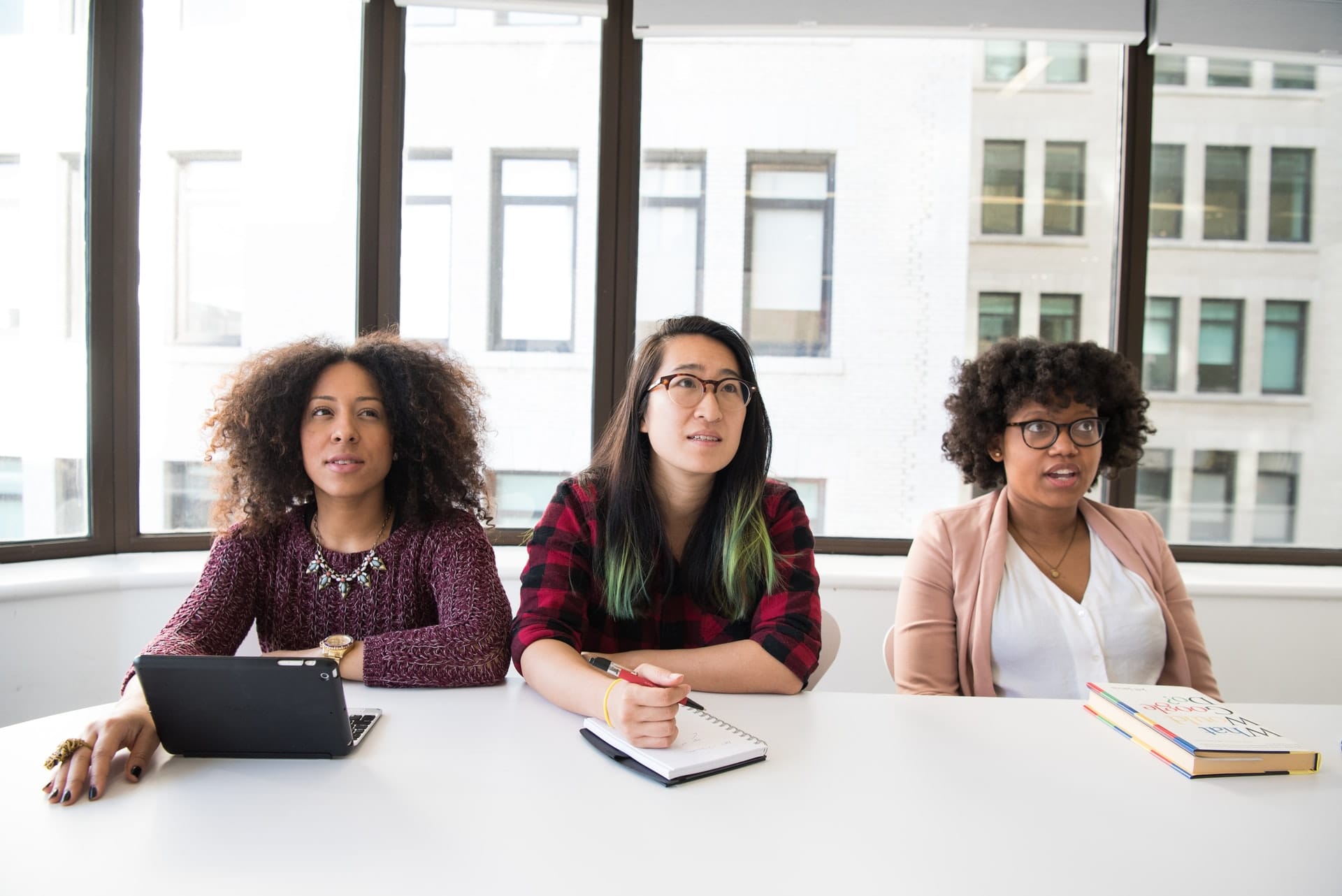 Three women of colour sitting in a meeting looking skeptical