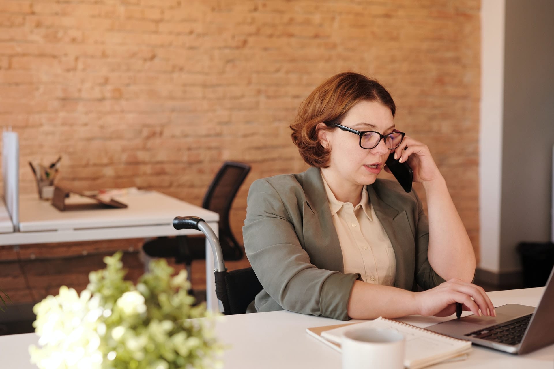Woman talking through smartphone while using laptop