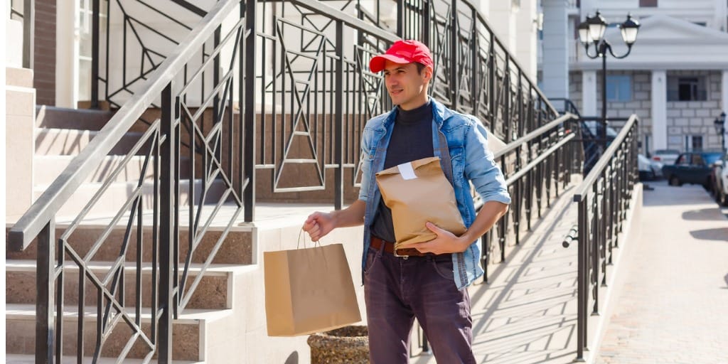 Man carrying two paper bags walking away from a building