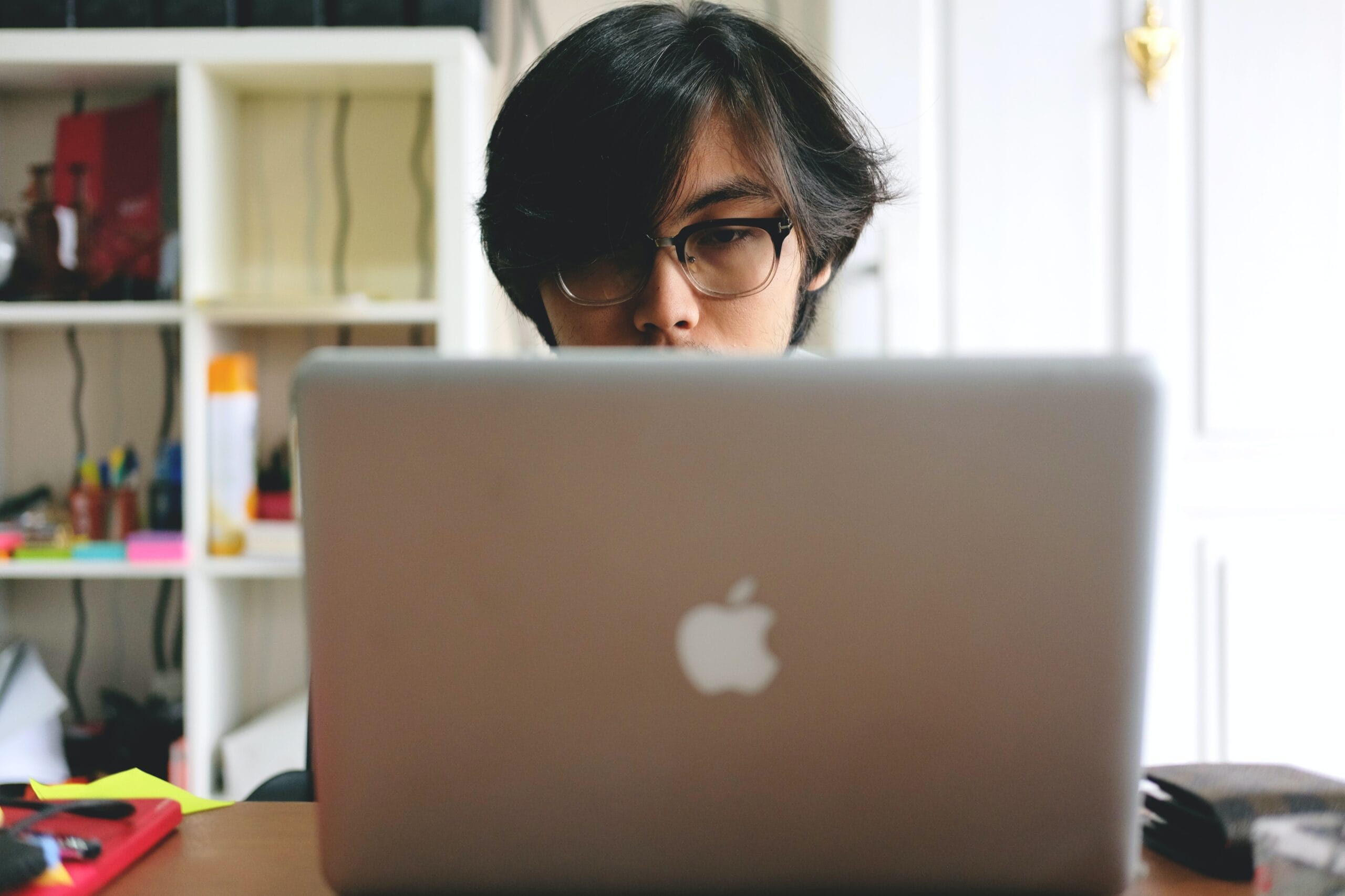 Person wearing glasses sitting behind a Macbook